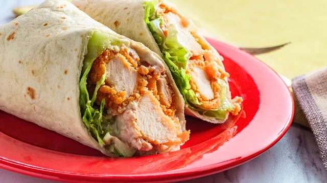 Buffalo Chicken Wraps with spicy chicken, fresh veggies, and creamy dressing on a marble countertop in a modern kitchen.