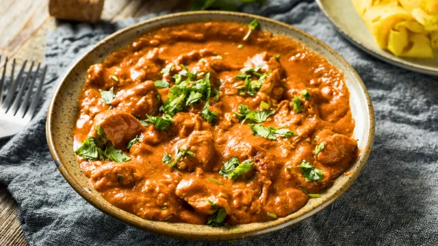 A bowl of Chicken Tikka Masala in a creamy, spiced tomato sauce on a marble countertop in a modern kitchen.