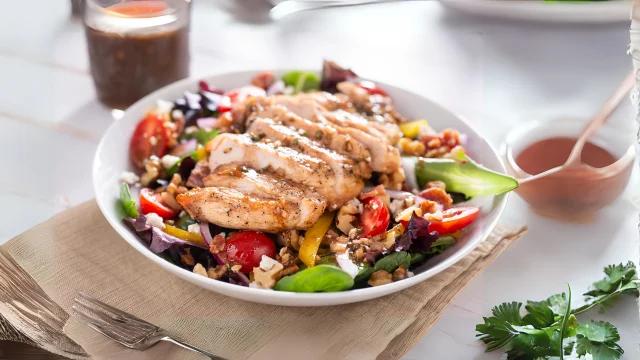A fresh Greek Chicken Salad with grilled chicken, vegetables, and tangy dressing on a marble countertop in a modern kitchen.