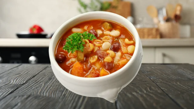 A bowl of hearty Minestrone Soup with vegetables, beans, and pasta on a marble countertop in a modern kitchen.