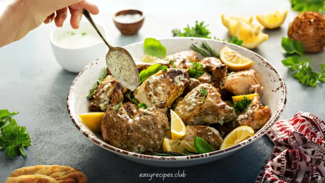 Golden brown One-Pan Lemon Garlic Chicken garnished with lemon slices and fresh herbs on a marble countertop in a modern kitchen.