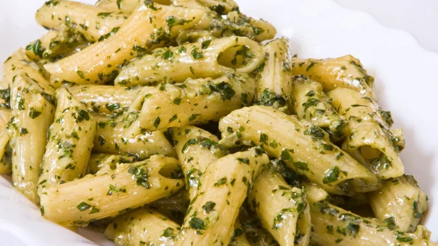 A plate of Pesto Penne pasta with fresh basil pesto sauce on a marble countertop in a modern kitchen.
