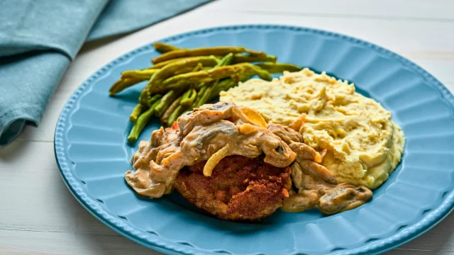 Salisbury Steak recipe; a blue plate topped with mashed potatoes, green beans and a meatloaf