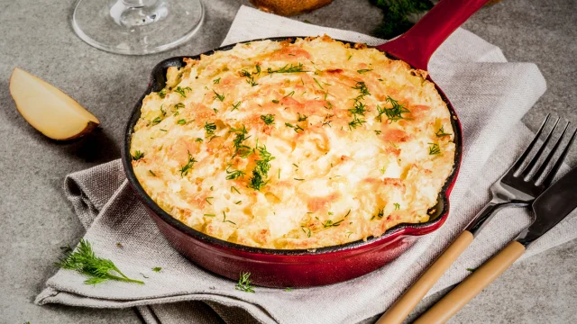 A dish of Shepherd’s Pie with savory meat and vegetable filling topped with golden mashed potatoes on a marble countertop in a modern kitchen.