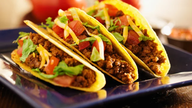 three ground beef tacos sitting on a blue plate on a wooden table